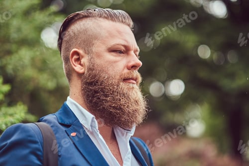Preview: Bearded male with a haircut dressed in a shirt and jacket with a backpack, standing in a park.