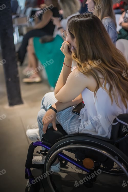 Preview: Girl in a wheelchair at a lecture or conference with colleagues listens to the lecturer