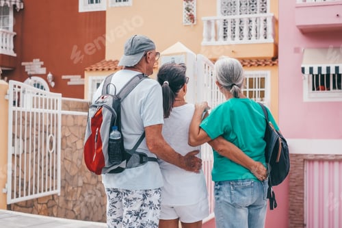 Preview: Group of three caucasian senior friends outdoors looking at pastel colored houses
