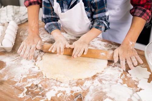 Preview: Hands of young female and little boy rolling dough while preparing cookies