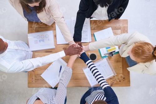 Preview: High angle shot of a group of colleagues standing around a desk with their hands in a huddle