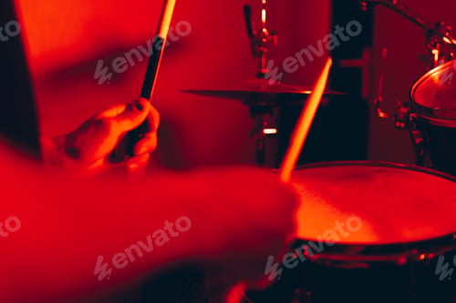 Preview: Anonymous man with drumsticks playing on drums in redness