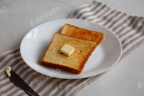 Preview: Homemade Toasted Bread Slice with Butter on a Plate, side view.