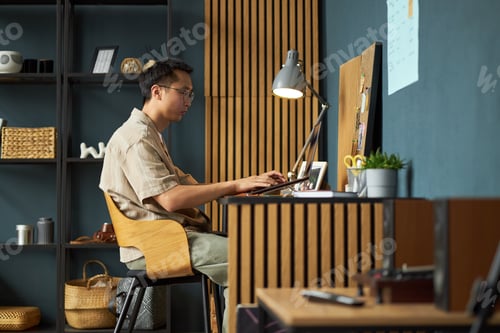 Preview: Young Adult Asian Man Working on Laptop at Modern Home Office Desk