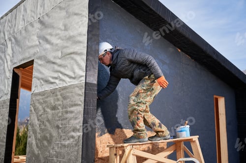 Preview: Male painter using paint roller, doing exterior paint work while building wooden frame house.