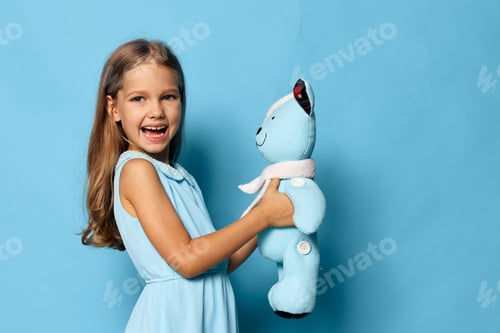 Preview: Little girl in blue dress holding matching blue teddy bear against a vibrant blue background