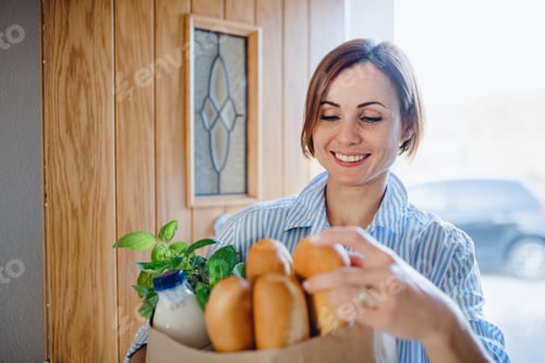 Preview: A young woman with groceries in paper shopping bag walking in through front door.