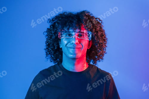 Preview: Young beautiful man with curly hair is indoors in the studio with neon lighting