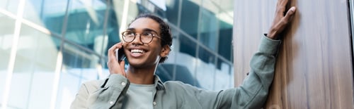 Preview: joyful african american man looking away while talking on mobile phone outdoors, banner