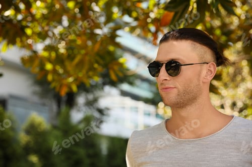Preview: Handsome young man in stylish sunglasses at park, space for text
