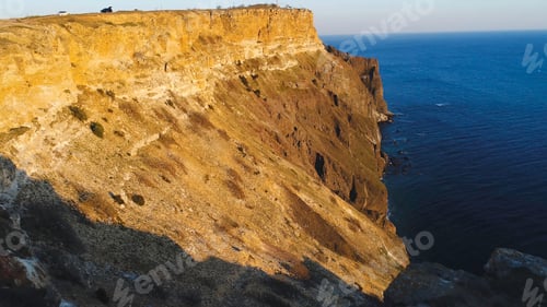 Preview: Top view of coastal cliff with blue sea at sunset. Shot. Beautiful view of golden sunset light on