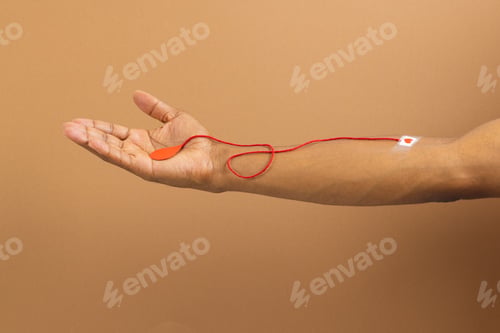 Preview: Arm of biracial man with heart sticking plaster and red string with blood drop, on brown background