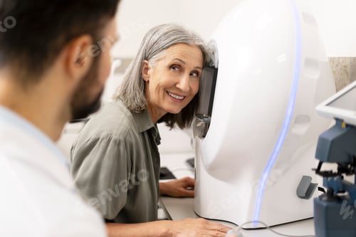 Preview: Senior woman undergoing eye exam with modern equipment and smiling doctor