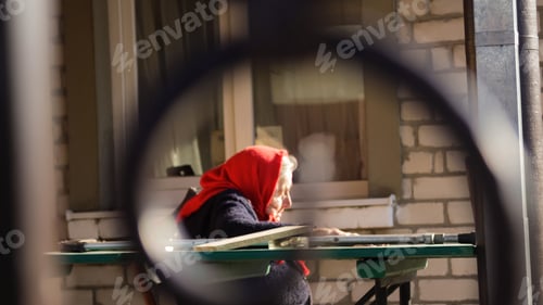 Preview: ukrainian elderly woman in red shawl with crutches sitting outside. Woman 85 years old. Alone person