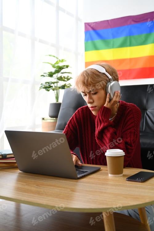 Preview: Focused young Asian gay man student in headphone looking at laptop screen.