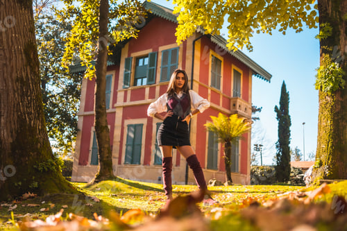Preview: a young Caucasian brunette college girl, in a park next to a red house enjoying the fall