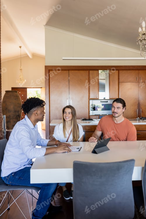Preview: Diverse friends discussing project at home, using tablet and documents on table