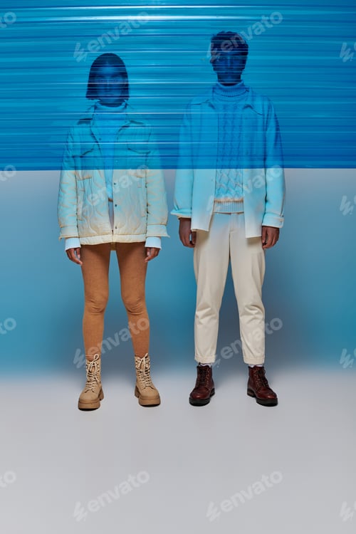 Preview: interracial couple in jackets and leather boots standing behind blue plastic panel, winter style