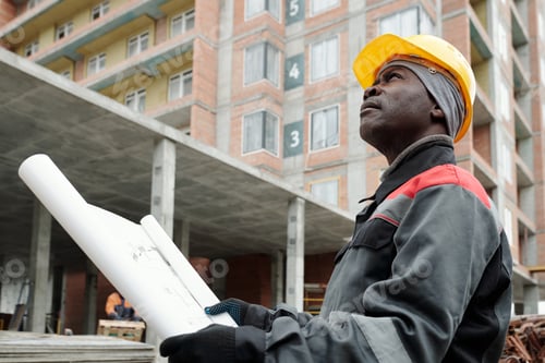 Preview: African American engineer in workwear looking upwards at highrise condo