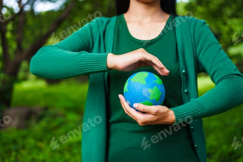 Preview: An Asian woman holds a globe in green forest,symbolizing importance preserving nature.emphasizes