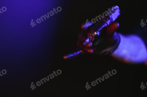 Preview: Closeup of tattooer master's hand in black glove holding machine for making tattoo