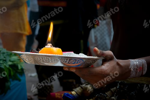 Preview: A devotee holding a silver ritual tray featuring a burning flame atop an orange and sacred ash.
