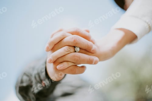 Preview: Low angle of a couple holding hands announcing their engagement and showing the ring