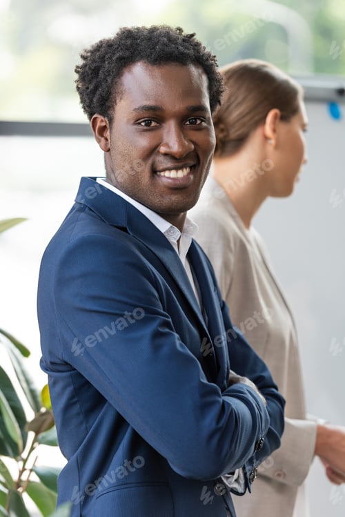 Preview: smiling african american businessman standing with crossed arms near colleague and looking at camera