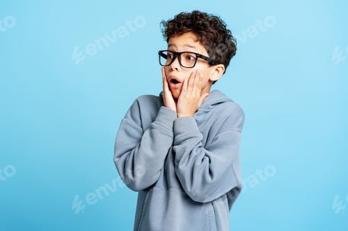 Preview: Scared unhappy little boy wearing stylish eyeglasses looking away isolated on blue background