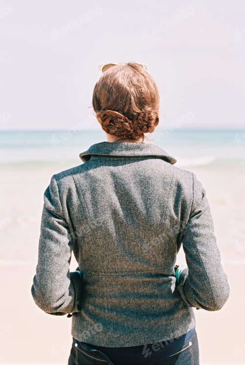 Preview: A woman in a grey jacket looking out over a beach and the sea.