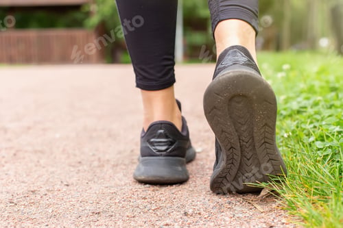Preview: Close-up of a womans legs, in black sneakers , walking along a path made of small red stone