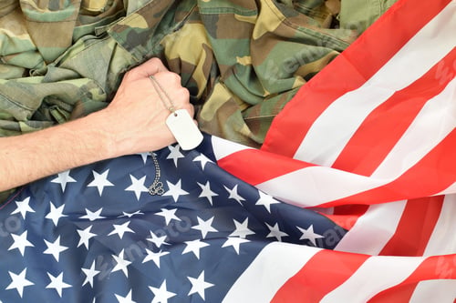 Preview: Male hand holds dog tag on USA flag and military uniform background