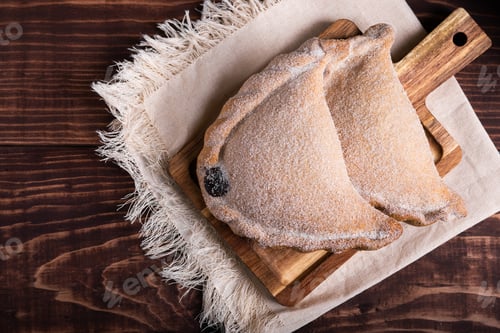 Preview: Close-up of two delicious empanadas dusted with sugar, resting on a rustic wooden board