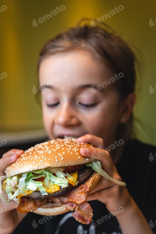 Preview: A little girl eats an appetizing burger, close-up.
