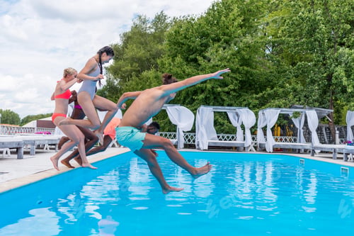 Preview: Group of beautiful young multiethnic people looking happy while jumping into the swimming pool