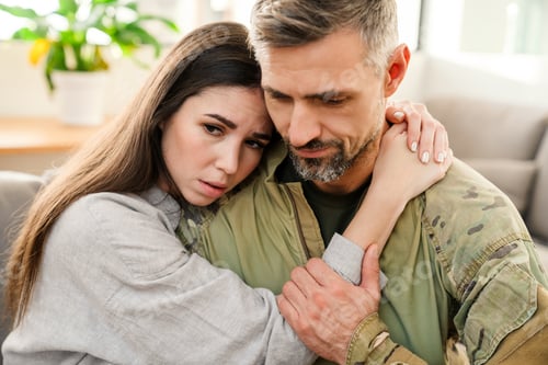 Preview: Unhappy woman hugging her military husband while sitting on sofa