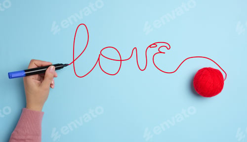 Preview: A woman's hand wrote love with a red felt-tip pen and a ball of wool
