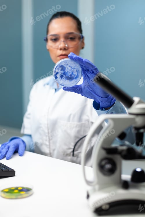 Preview: Biochemist researcher woman holding petri dish analyzing blue solution
