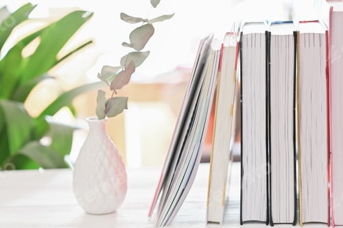 Preview: Close up view of workspace with books and ceramic vase on white desk.