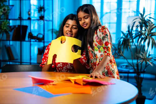 Preview: Indian sisters doing paper craft with scissors during fun and focused indoor art session