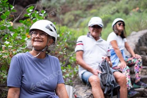 Preview: Happy group of seniors hikers with protective helmets resting during excursion in mountain