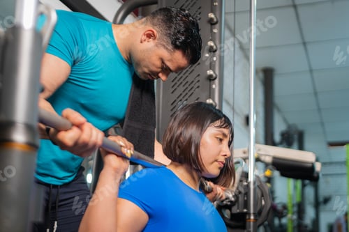 Preview: Personal trainer assisting determined woman lifting weights in gym