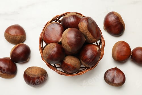 Preview: Sweet fresh edible chestnuts in wicker bowl on white table, top view