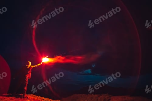 Preview: The man with a red firework stick standing on a night mountain.