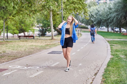 Preview: Young caucasian woman with blonde hair walks outdoors in a park