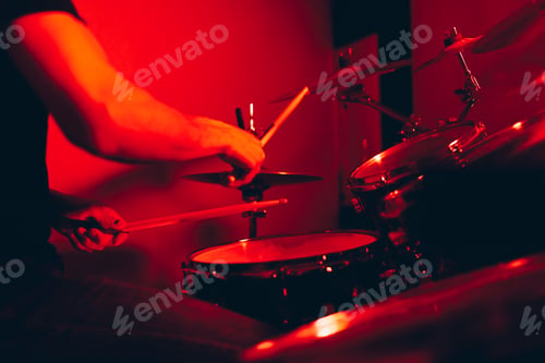 Preview: Anonymous man with drumsticks playing on drums in redness