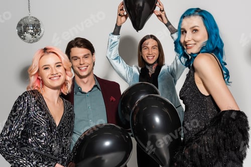 Preview: cheerful queer person holding black balloon above head near nonbinary friends smiling at camera on