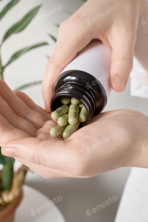 Preview: Female hands pouring green herbal capsules from bottle into palm showing wellness