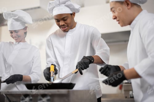 Preview: Multiracial team of professional cooks in uniform preparing meals for a restaurant in the kitchen