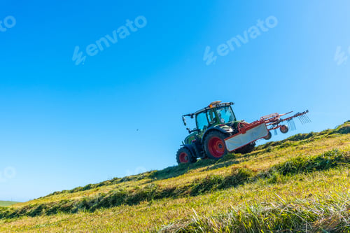 Preview: A tractor is driving down a hill, plowing the grass
